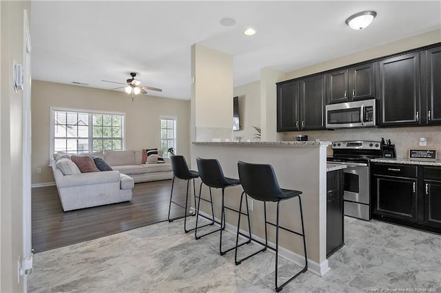 kitchen featuring stainless steel appliances, a kitchen breakfast bar, ceiling fan, baseboards, and dark cabinetry