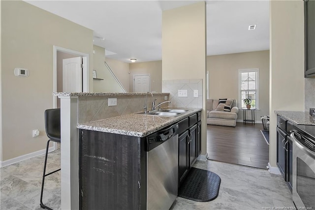 kitchen with appliances with stainless steel finishes, a sink, backsplash, and light stone counters