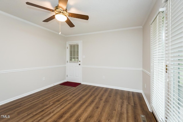 spare room with dark wood-type flooring, plenty of natural light, ceiling fan, crown molding, and baseboards