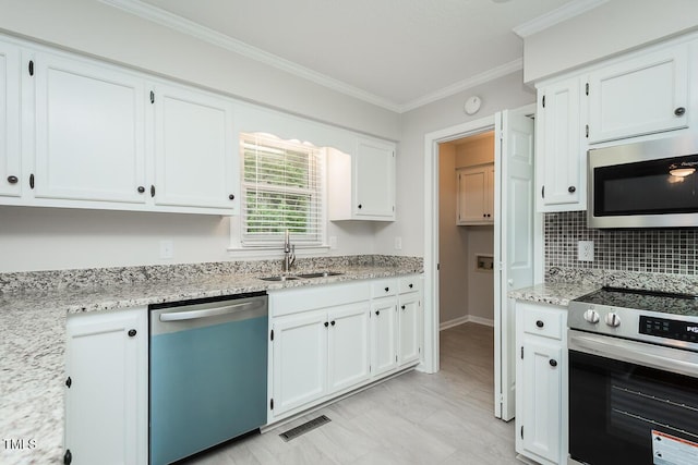kitchen with appliances with stainless steel finishes, a sink, crown molding, white cabinetry, and light stone counters