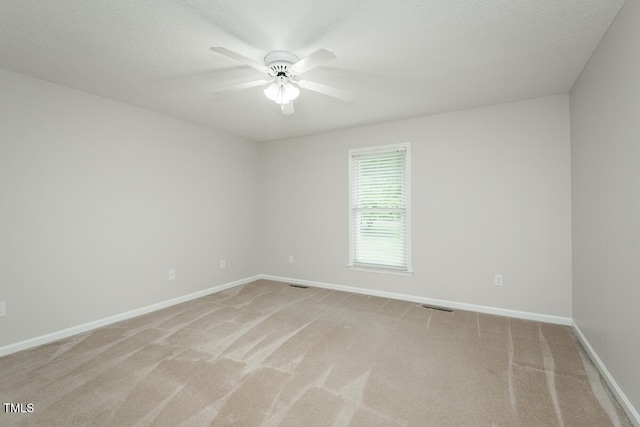 empty room featuring a ceiling fan, light colored carpet, baseboards, and a textured ceiling