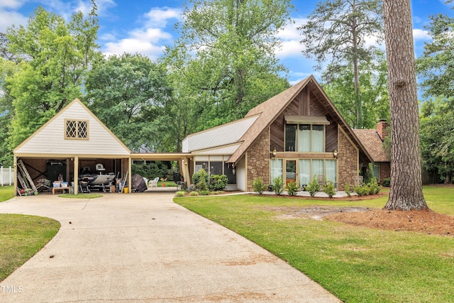 a-frame style home featuring stone siding, a front yard, a chimney, concrete driveway, and a carport