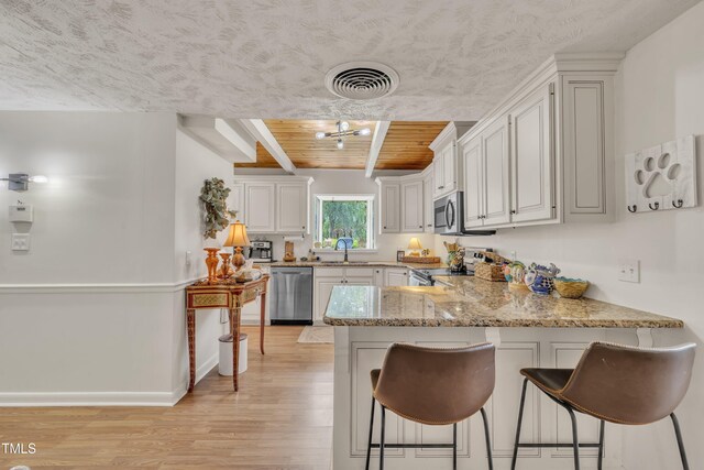kitchen featuring stainless steel appliances, a sink, light wood-style flooring, a peninsula, and a kitchen bar