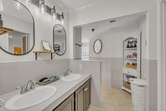 bathroom with tile walls, ornamental molding, double vanity, and a wainscoted wall