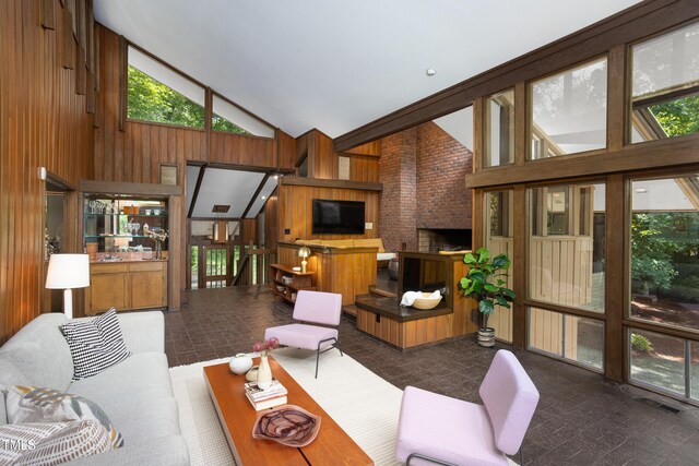 living area featuring high vaulted ceiling, wood walls, and a brick fireplace