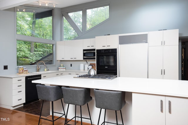 kitchen with black appliances, a sink, light countertops, white cabinetry, and a high ceiling