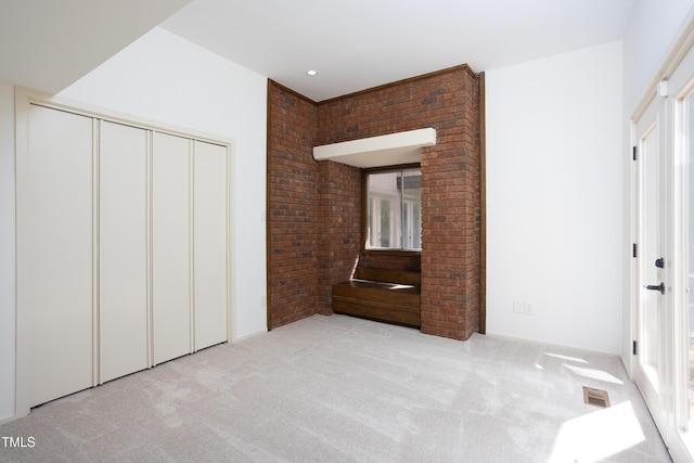 unfurnished bedroom with light carpet, a closet, multiple windows, and brick wall