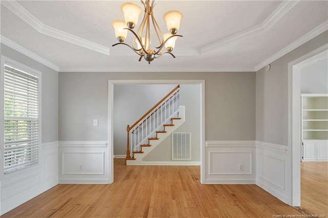empty room with a chandelier, wood finished floors, stairs, ornamental molding, and wainscoting