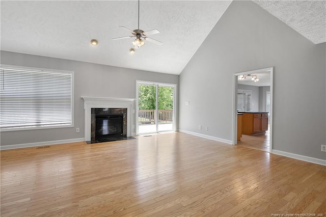 unfurnished living room featuring a ceiling fan, a textured ceiling, high vaulted ceiling, light wood-type flooring, and a high end fireplace