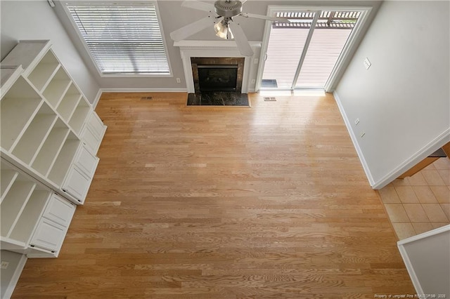 unfurnished living room with ceiling fan, light wood-type flooring, baseboards, and a high end fireplace