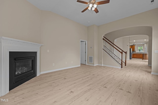1020 Kingston Grove Dr, Cary, NC 27519 - unfurnished living room with arched walkways, stairs, light wood-style floors, ceiling fan, and a glass covered fireplace