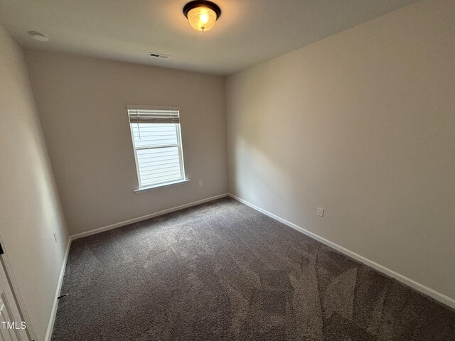 spare room featuring dark colored carpet and baseboards