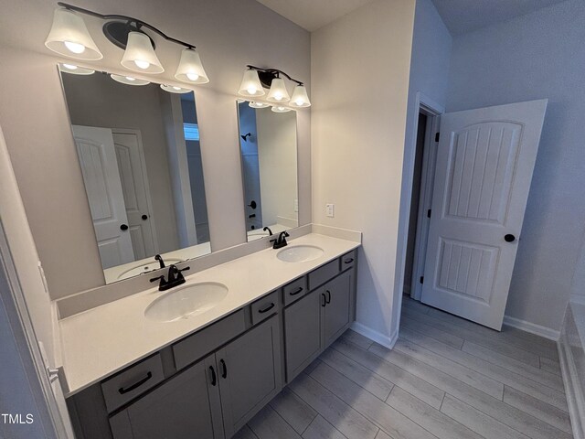 full bath featuring wood finished floors, double vanity, and baseboards