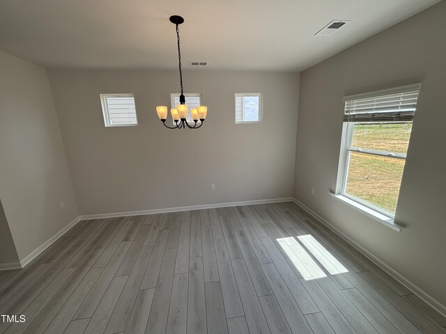 unfurnished dining area featuring wood finished floors, a chandelier, and baseboards