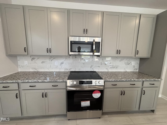kitchen with appliances with stainless steel finishes, gray cabinetry, tasteful backsplash, and light stone countertops