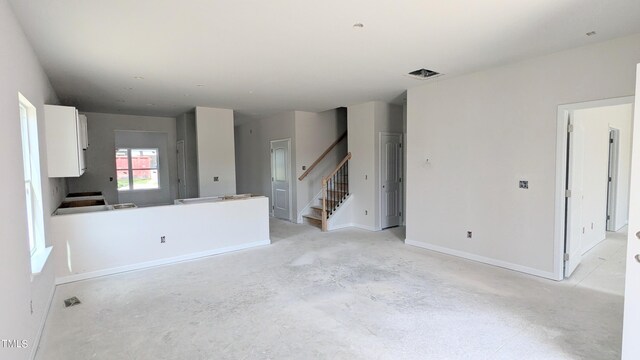 unfurnished living room with stairs, unfinished concrete floors, and baseboards