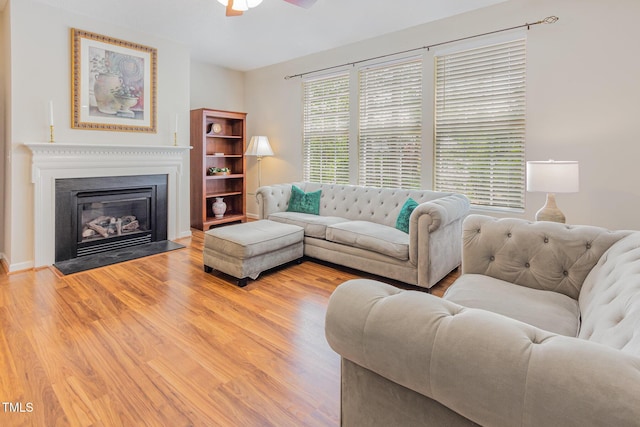 living area featuring light wood finished floors, a ceiling fan, and a fireplace with flush hearth