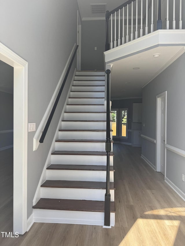 staircase with wood finished floors, ornamental molding, and baseboards