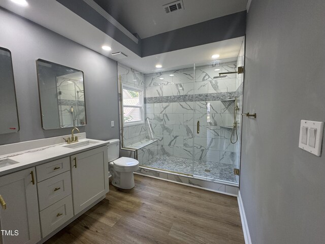 bathroom featuring toilet, recessed lighting, a marble finish shower, wood finished floors, and double vanity
