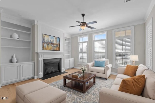 living room featuring light wood-style floors, ceiling fan, ornamental molding, a fireplace with flush hearth, and built in shelves