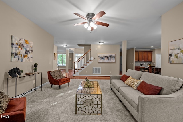 living area with ceiling fan, stairway, baseboards, and carpet