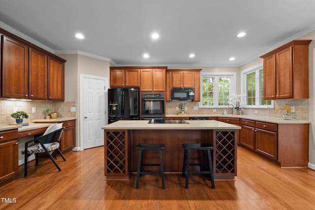 kitchen featuring black appliances, ornamental molding, decorative backsplash, light wood-style floors, and light countertops