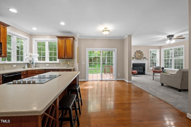 kitchen with black appliances, a sink, a kitchen bar, a glass covered fireplace, and brown cabinets