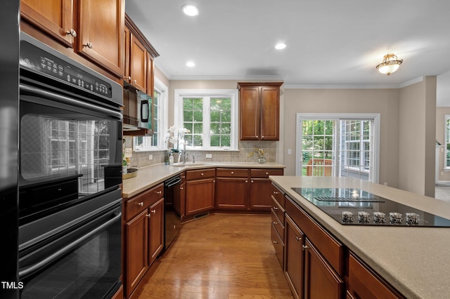 kitchen featuring black appliances, ornamental molding, light wood-style floors, tasteful backsplash, and healthy amount of natural light