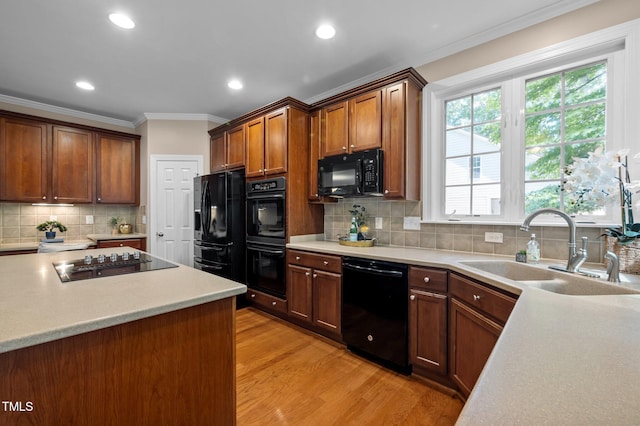 kitchen with black appliances, a sink, light wood finished floors, crown molding, and light countertops