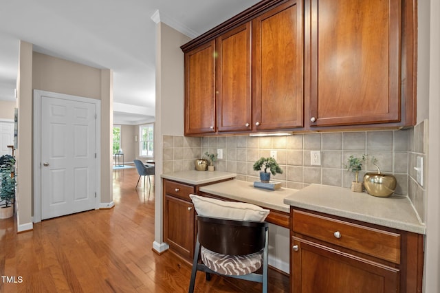 kitchen featuring wood finished floors, backsplash, light countertops, and crown molding
