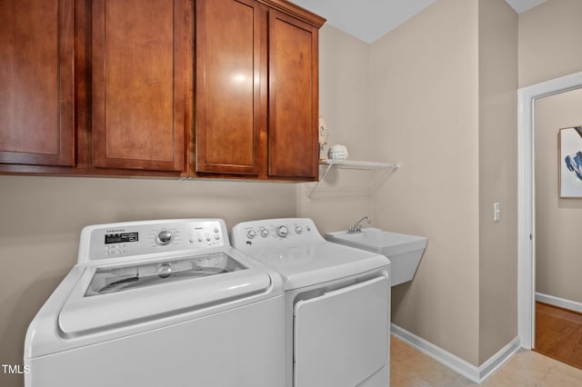 clothes washing area with washing machine and clothes dryer, baseboards, and cabinet space