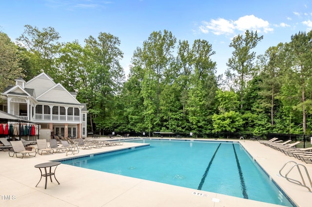 community pool with a patio area and view of wooded area