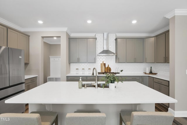kitchen featuring wall chimney range hood, freestanding refrigerator, gray cabinets, a breakfast bar area, and ornamental molding