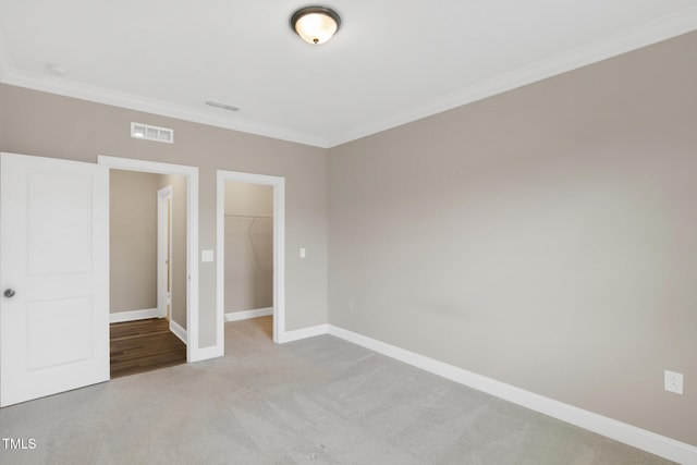 unfurnished bedroom featuring crown molding, carpet floors, a walk in closet, baseboards, and a closet