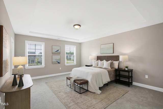 carpeted bedroom featuring a raised ceiling and baseboards