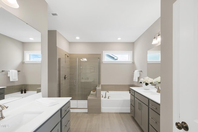 bathroom with plenty of natural light, a stall shower, two vanities, a bath, and recessed lighting