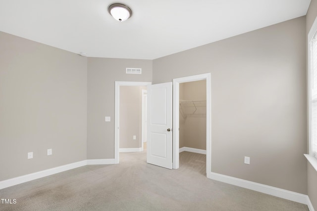 unfurnished bedroom featuring light colored carpet, a spacious closet, a closet, and baseboards