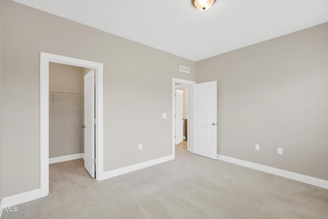 unfurnished bedroom with light carpet, a spacious closet, and baseboards