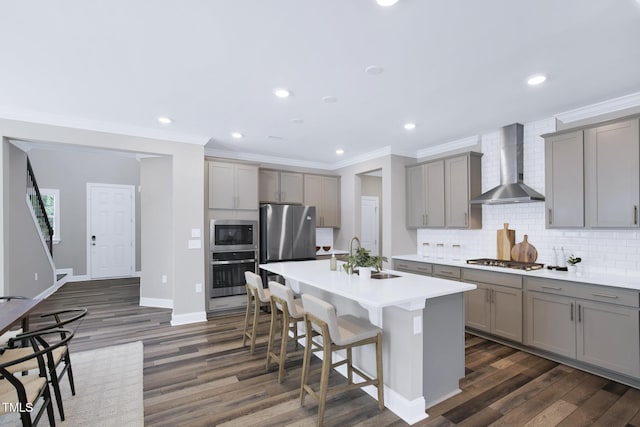 kitchen with gray cabinetry, appliances with stainless steel finishes, wall chimney exhaust hood, a sink, and dark wood-style floors