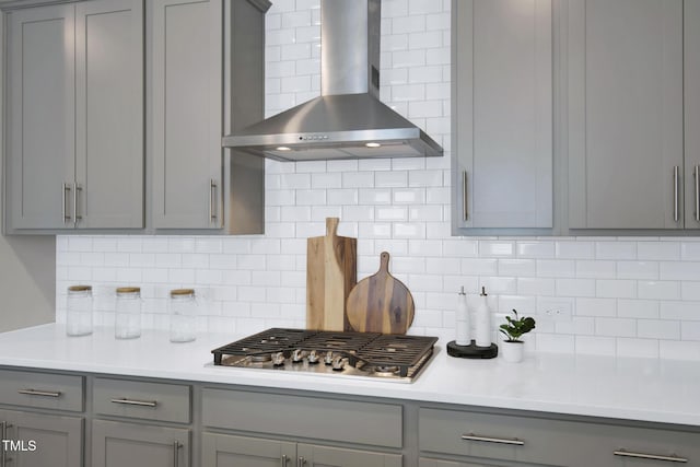 kitchen with gray cabinets, wall chimney exhaust hood, stainless steel gas cooktop, backsplash, and light countertops