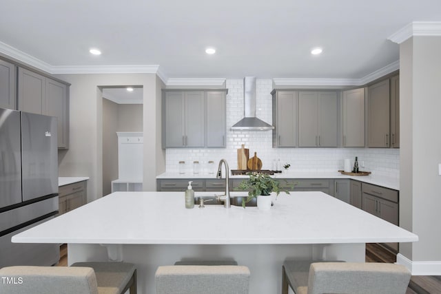 kitchen with wall chimney exhaust hood, gray cabinetry, freestanding refrigerator, a kitchen breakfast bar, and crown molding