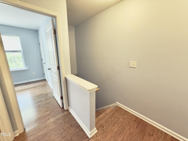 hall featuring wood finished floors, baseboards, and an upstairs landing