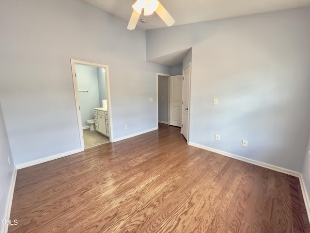 unfurnished bedroom featuring baseboards, wood finished floors, ensuite bathroom, high vaulted ceiling, and a ceiling fan