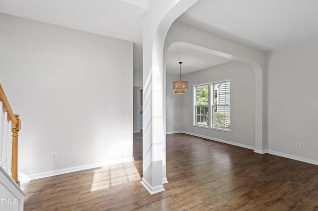unfurnished living room featuring arched walkways, dark wood finished floors, baseboards, and a chandelier