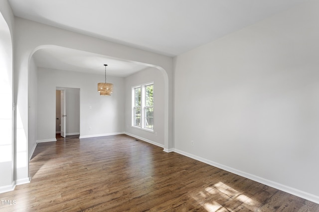 spare room featuring arched walkways, a chandelier, dark wood-style flooring, and baseboards