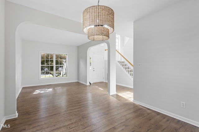 unfurnished living room with arched walkways, a chandelier, wood finished floors, baseboards, and stairway