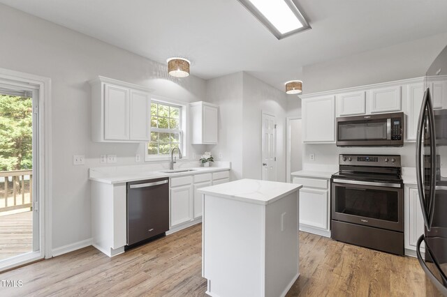 kitchen featuring appliances with stainless steel finishes, a sink, white cabinets, a kitchen island, and light wood-style floors