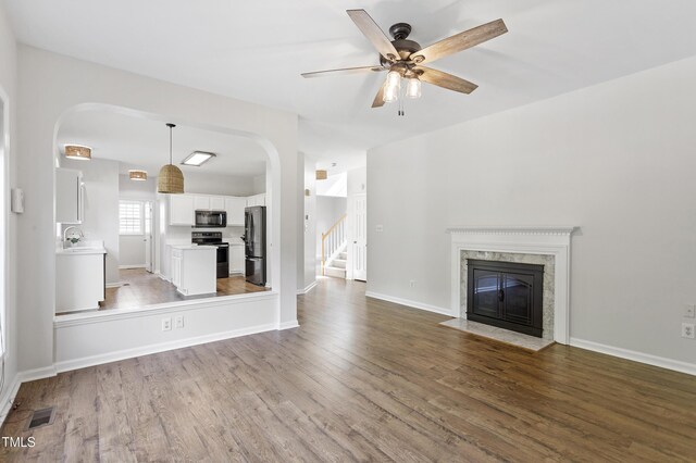 unfurnished living room featuring arched walkways, a ceiling fan, and wood finished floors