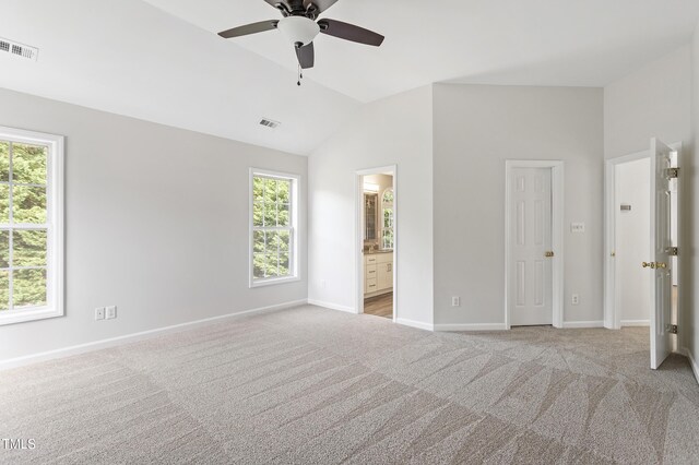 unfurnished bedroom with lofted ceiling, light colored carpet, multiple windows, baseboards, and ensuite bath