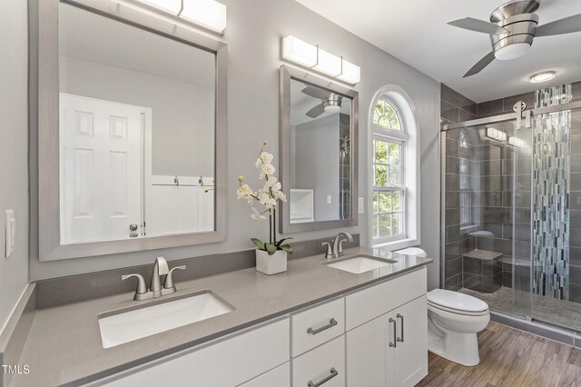 bathroom with toilet, a stall shower, double vanity, a ceiling fan, and wood finished floors